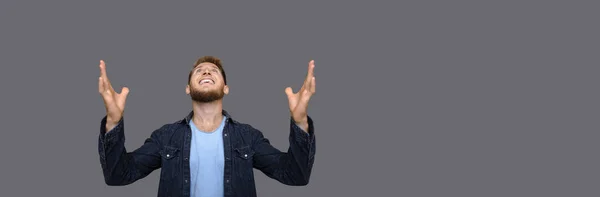 Homem caucasiano está olhando para cima e agradecendo a Deus por algo enquanto posando em uma parede de estúdio cinza com espaço livre — Fotografia de Stock