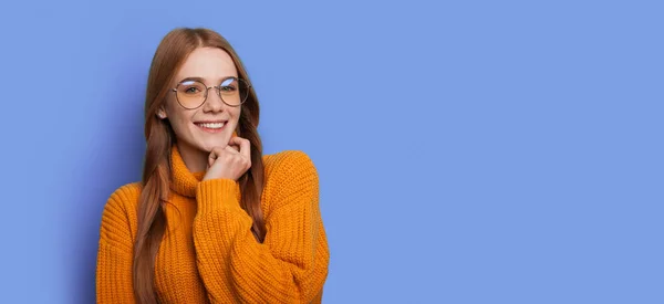 Zázvorová žena s rudými vlasy se usmívá na kameru s brýlemi na modré zdi studia s volným místem — Stock fotografie