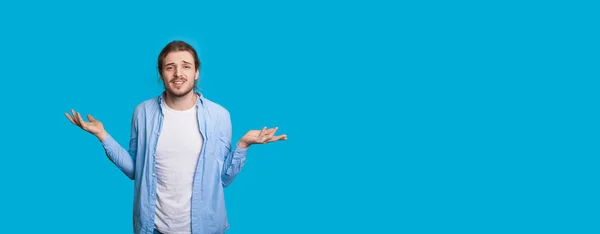 Hombre caucásico con barba y pelo largo haciendo gestos de confusión en una pared azul con espacio libre — Foto de Stock