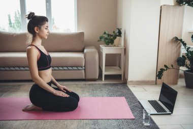 Kafkasyalı bir kadın dizüstü bilgisayarın önünde oturuyor ve spor kıyafetleri içinde su olan bir cam ve online fitness dersine hazırlanıyor.