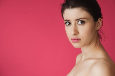 Çilli, çıplak omuzlu, pembe arka planda poz veren beyaz kadın kameraya bakıyor.