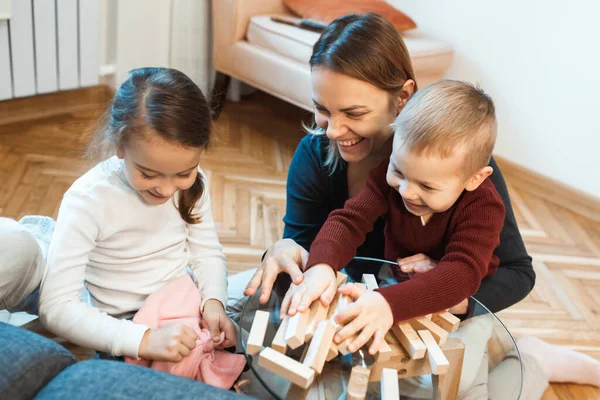 Madre caucasica e bambini che giocano con il costruttore di legno sul tavolo di vetro insieme divertendosi — Foto Stock