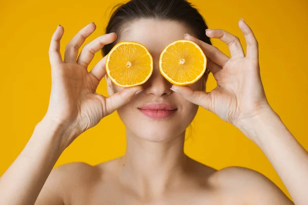Белая женщина с голыми плечами, позирующая на желтой стене студии, закрывая глаза лимоном — стоковое фото