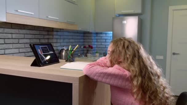 Schattig schoolmeisje met blond krullend haar is het hebben van online les met behulp van een tablet, terwijl het kijken naar de leraar uitleggen van de les — Stockvideo