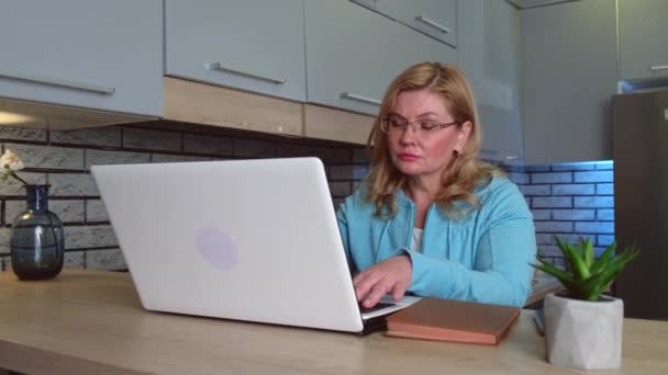 Geconcentreerde blanke senior vrouw is het drinken van een koffie tijdens het werken op de laptop in de woonkamer kijken naar het scherm — Stockvideo