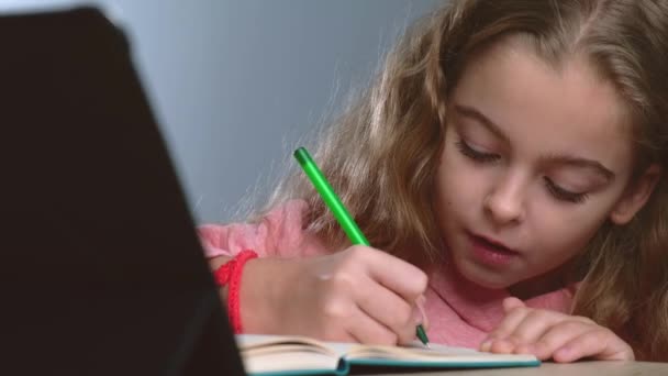 Menina concentrada está tendo aula on-line usando um tablet e escrever as notas no caderno — Vídeo de Stock