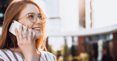 Kızıl saçlı ve gözlüklü genç girişimci telefonda konuşuyor ve gülümsüyor.