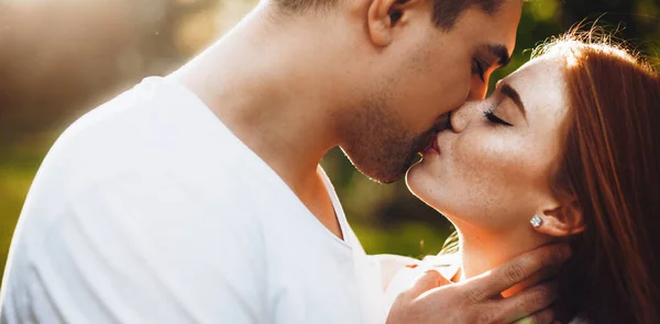 Nahaufnahme Foto einer kaukasischen Dame mit Sommersprossen und Ingwerhaaren, die ihren Liebhaber küsst und sich an einem sonnigen Tag im Park umarmt — Stockfoto