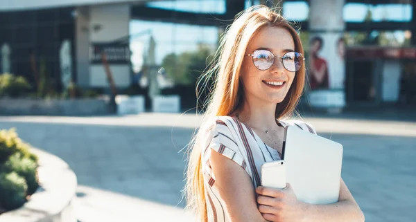 Kaukasische Geschäftsfrau mit roten Haaren und Sommersprossen mit Brille posiert draußen mit Laptop und Handy — Stockfoto