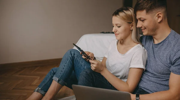 Прекрасна біла пара сидить на підлозі і використовує ноутбук і планшет — стокове фото