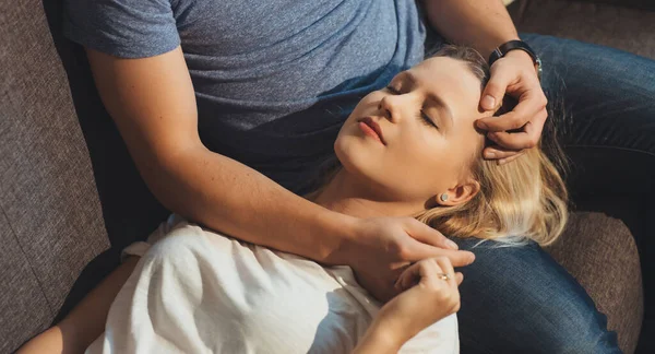 De cerca foto de una mujer caucásica con el pelo rubio acostado en sus amantes rodillas con los ojos cerrados en el sofá —  Fotos de Stock