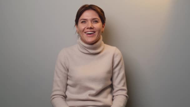 Estúdio de vídeo de uma mulher caucasiana sorrindo para a câmera em uma parede cinza vestindo uma camisola quente — Vídeo de Stock