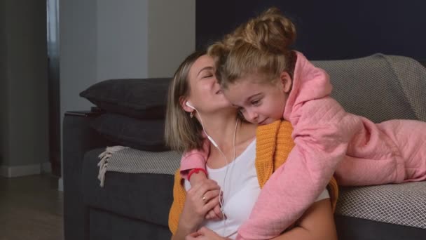 Caucásica madre besando a su hija mientras escucha música en los auriculares sonriendo y abrazándola — Vídeo de stock