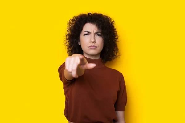 Droevige krullenbol vrouw wijst naar camera op een gele muur gebaren van ongeluk — Stockfoto