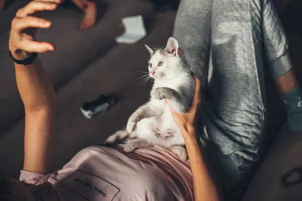 Kaukasische Frau liegt im Bett, hält ihre Katze und spielt mit ihr und gestikuliert mit der Hand — Stockfoto