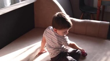 Küçük çocuk koltukta arabasıyla oynuyor. Yalnızken araba sürüyormuş gibi yapıyor.