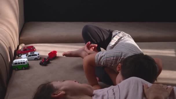 Kaukasischer Junge spielt mit seiner Mutter und ihrer Hand in der Nähe von Autospielzeug auf der Couch — Stockvideo