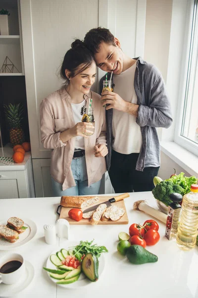 Coppia adorabile sorridente mentre beve succo fresco e mangia verdura in cucina — Foto Stock