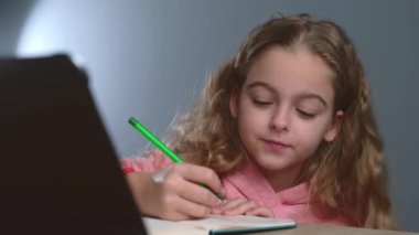 Kafkasyalı bir kızın defterine bir şey çizip tablet ekranından izlediği videoyu kapat.