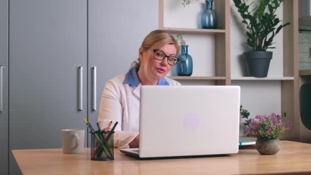 Médico sênior no escritório está usando um laptop para se conectar remotamente com os pacientes — Vídeo de Stock