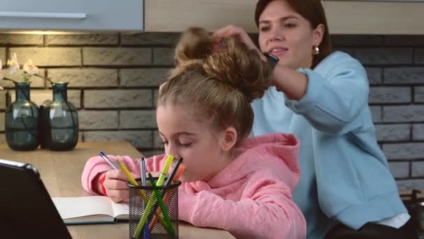 Careful mother is correcting her daughters hair while the girl is drawing and using a tablet — Stock Video