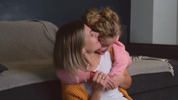 Mujer caucásica escuchando música mientras su hija la abraza — Vídeo de stock