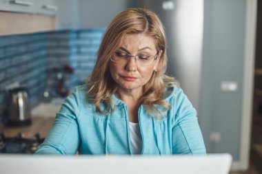 Üst düzey sarışın kadın evde çalışmaya odaklanmış durumda. Mutfakta uzaktan kumandalı gözlük takıyor.