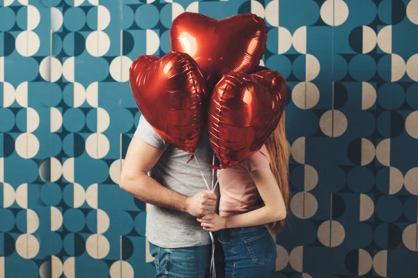 Fehér pár csókolózik a lufik mögött egy kék falon, Valentin-napot ünnepelve. — Stock Fotó