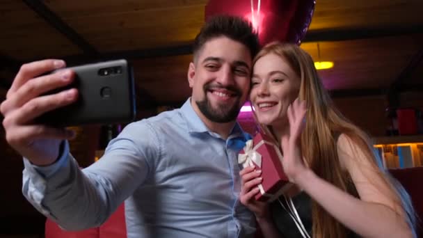 L'uomo caucasico con la barba sta facendo un selfie con la sua ragazza usando un telefono e tenendo palloncini rossi durante un appuntamento — Video Stock