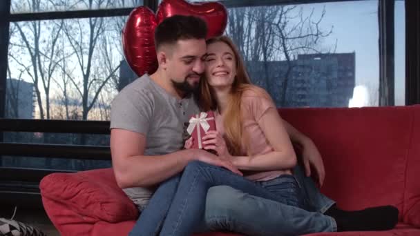Pareja caucásica sentada en el sofá y besándose celebrando el día de San Valentín dando regalos y globos — Vídeos de Stock