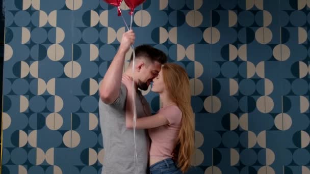Běloch drží balónky a zakrývá s nimi tvář, zatímco líbá svou zrzavou přítelkyni během Valentýna — Stock video