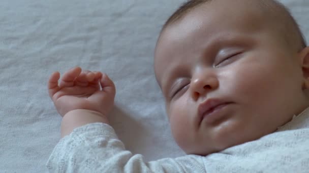 Primer plano de vídeo de una niña recién nacida caucásica durmiendo en la cama en una manta blanca y soñando con algo — Vídeo de stock