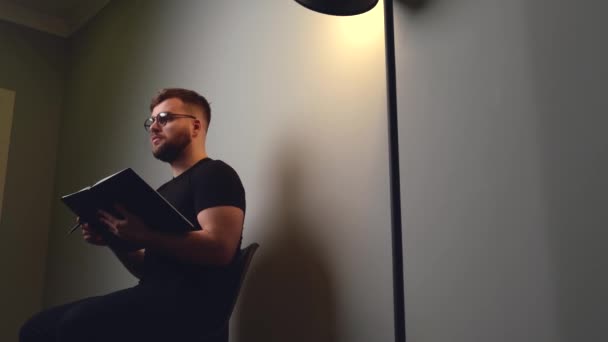 Fehér férfi szakállal olvas egy könyvből, miközben pózol egy szürke stúdió falán az online találkozó során — Stock videók