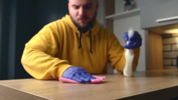 Hombre caucásico está limpiando una mesa en casa con guantes y el uso de aerosol antibacteriano — Vídeos de Stock