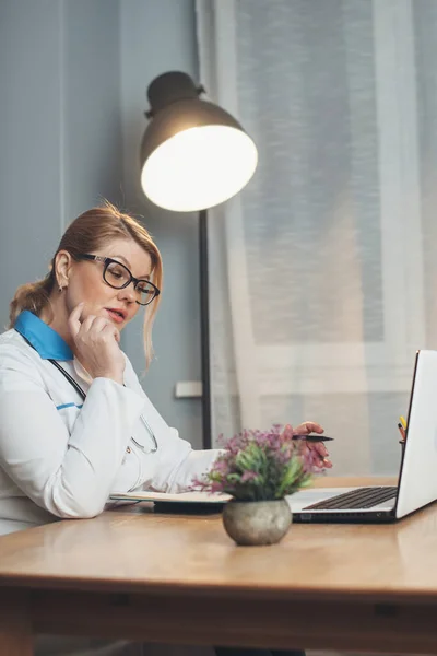 Senior doctor working from home is having online meeting with the patient using a laptop and wearing medical clothes and tools — Stock Photo, Image