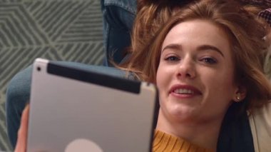 Kızıl kadın ona bakıp gülümserken dizlerinin üzerine çöküp tablet tutuyor.