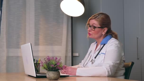 Video von einem kaukasischen Arzt in medizinischem Mantel, der auf dem Laptop mit dem Patienten spricht und ihm die Behandlungsschritte erklärt — Stockvideo