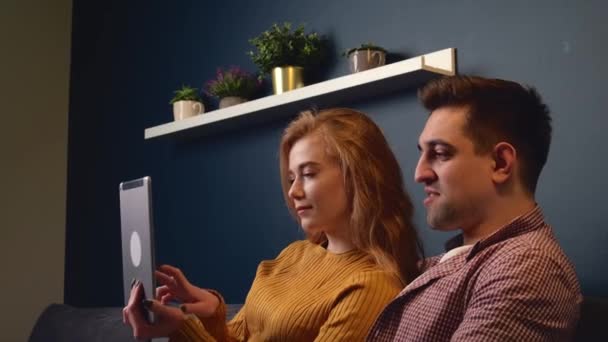 Vista lateral de vídeo de una pareja caucásica acostada en un sofá y viendo algo en una tableta — Vídeos de Stock