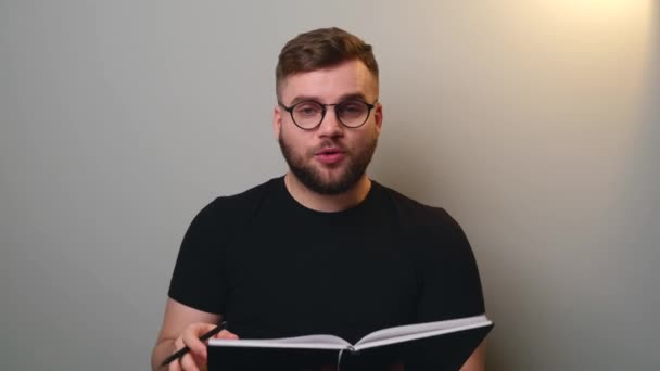 Kaukázusi férfi szakállas és szemüveges olvas egy könyvet a kamera online video hívás során — Stock videók