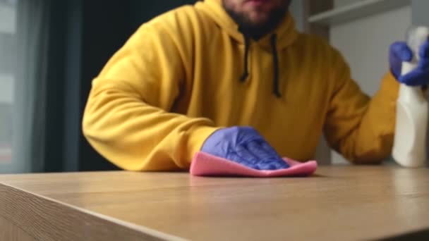 Caucásico barbudo hombre con guantes está limpiando la mesa con spray antibacteriano — Vídeos de Stock