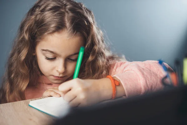 Foto de cerca de una chica rubia con el pelo ondulado escribiendo el tema en el cuaderno durante las clases en línea —  Fotos de Stock