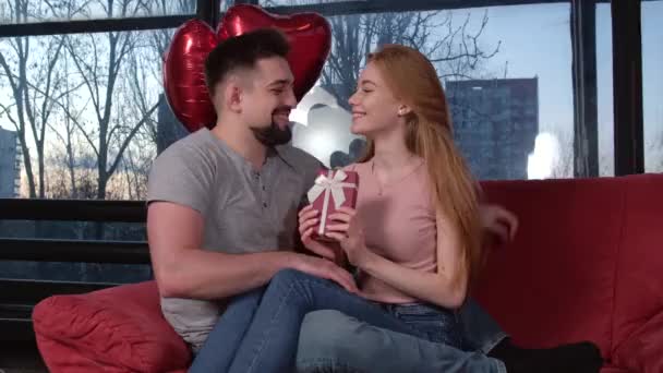 La coppia caucasica è seduta su un divano e sorride festeggiando il giorno di San Valentino con palloncini d'aria e presente — Video Stock