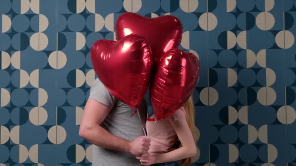 白种人夫妻躲藏在心形气球后面，亲吻着蓝色的工作室墙壁 — 图库视频影像
