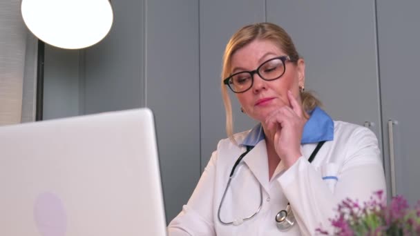 Kaukaski starszy medyk słucha i rozmawia z pacjentem przez Internet za pomocą laptopa w biurze — Wideo stockowe