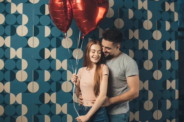 풍선을 들고 발렌틴 데이 데이트를 하는 파란 스튜디오 벽에서 포옹하는 커플 — 스톡 사진