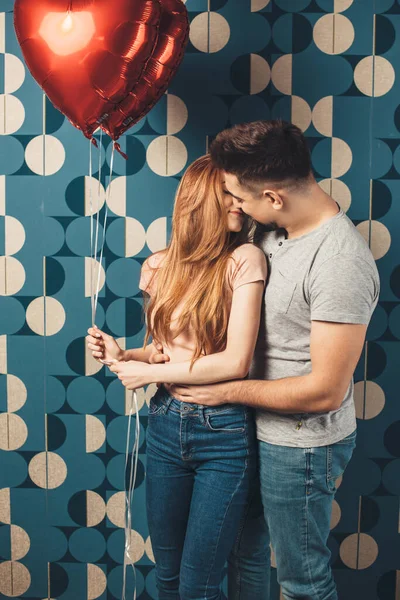 可愛いですカップル受け入れます上の青いスタジオ壁上のバレンタインデー保持赤い空気風船とキス — ストック写真