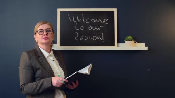 Professeur principal a une leçon devant la classe près du tableau noir avec un livre ouvert — Video