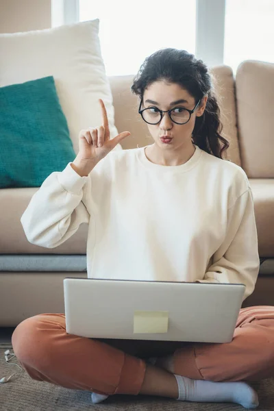 Kıvırcık saçlı kadın dizüstü bilgisayarında yerde online dersler verirken fikir işareti yapıyor. — Stok fotoğraf