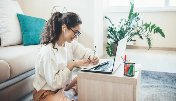 Kaukasiska kvinna gör online lektioner på laptop ler medan du skriver något sitter på golvet — Stockfoto