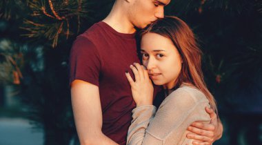 Çekici beyaz kadın erkek arkadaşının üzerine uzanmış ve kameraya gülümsüyor. Adam onu mükemmel bir günbatımında öperken.